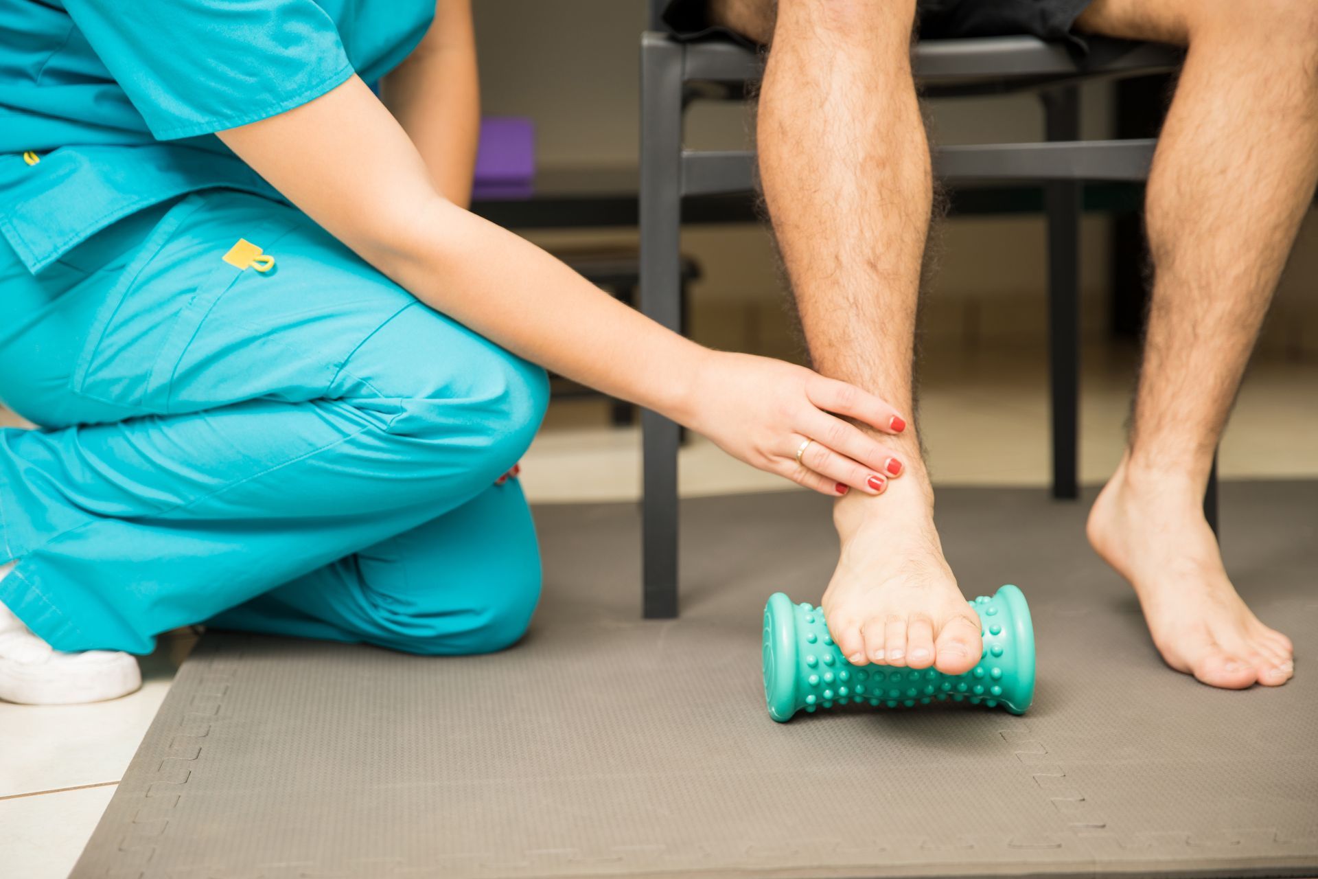 A nurse is kneeling down next to a patient 's foot while using a foot roller.