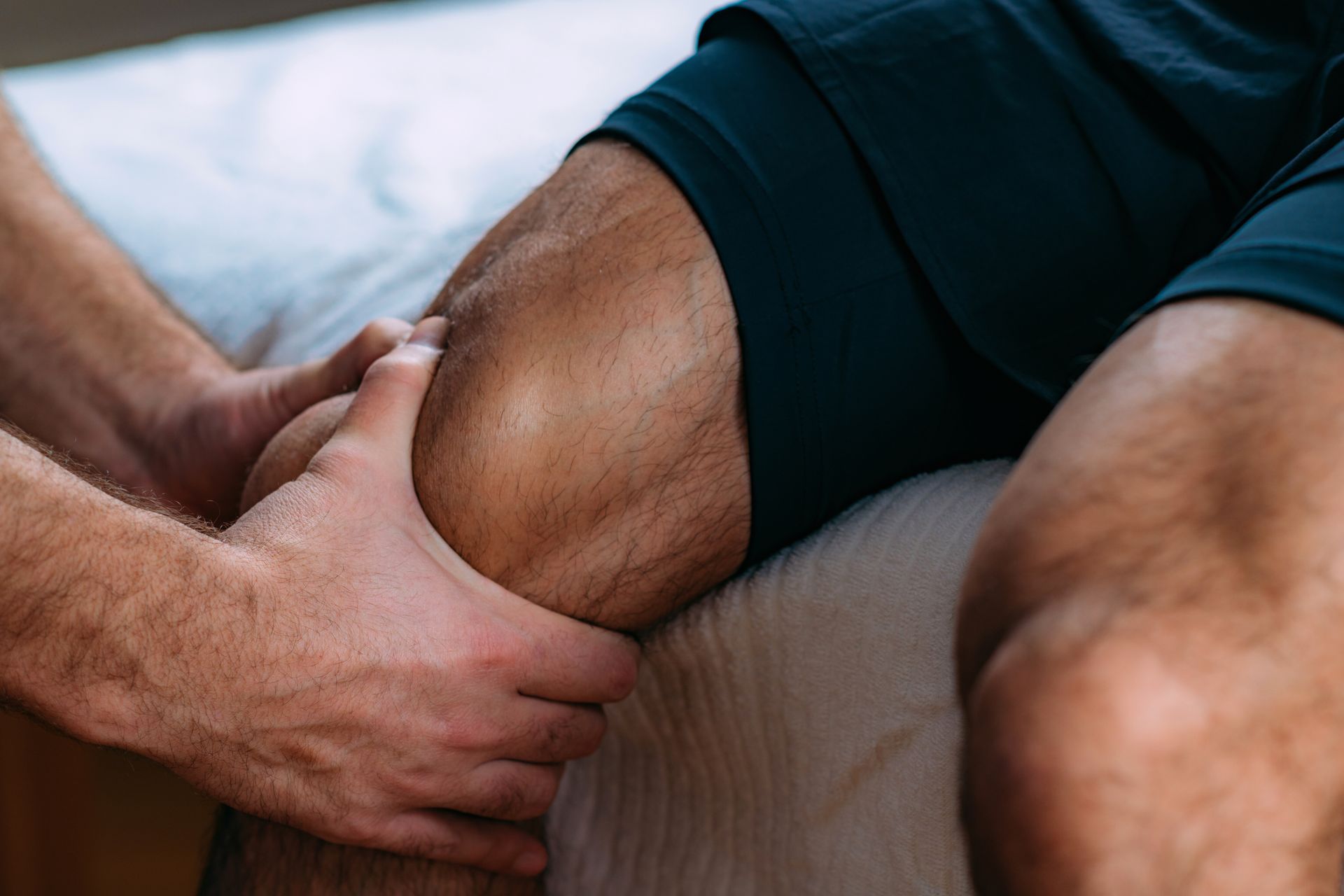 A man is getting a massage on his leg while sitting on a bed.