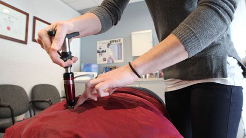 A woman is using a device on a man 's back.