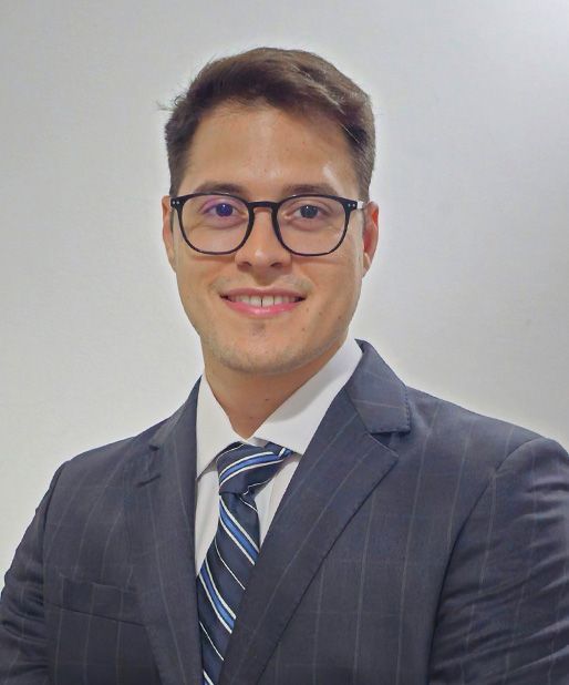 Man in suit and glasses smiles at the camera; white background.