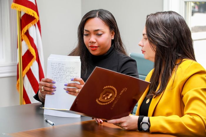 Two women reviewing documents at a table, one with a yellow blazer, the other with a black shirt.