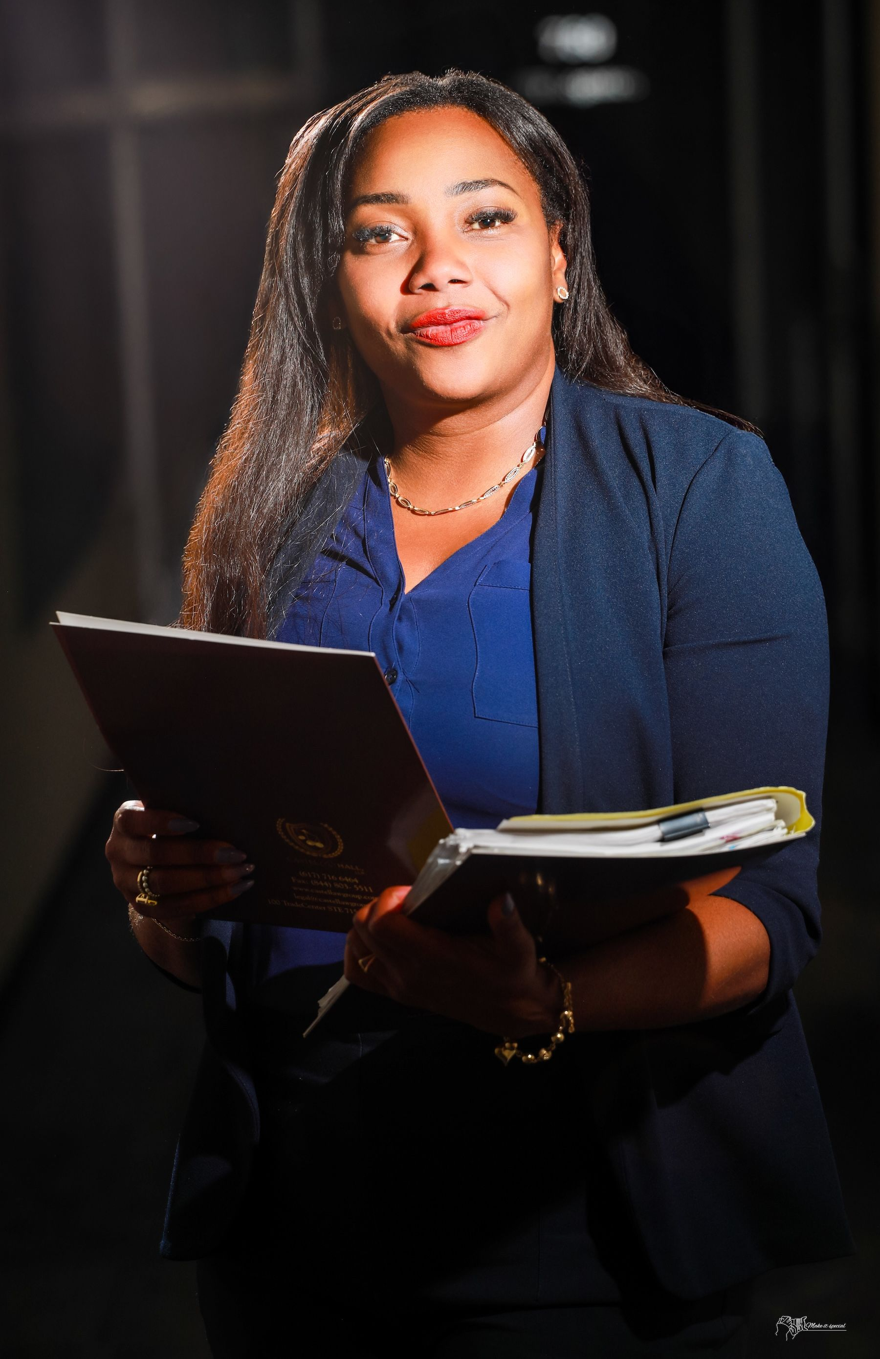Woman in a burgundy suit smiles, a silver necklace, indoors, with framed art on the wall.