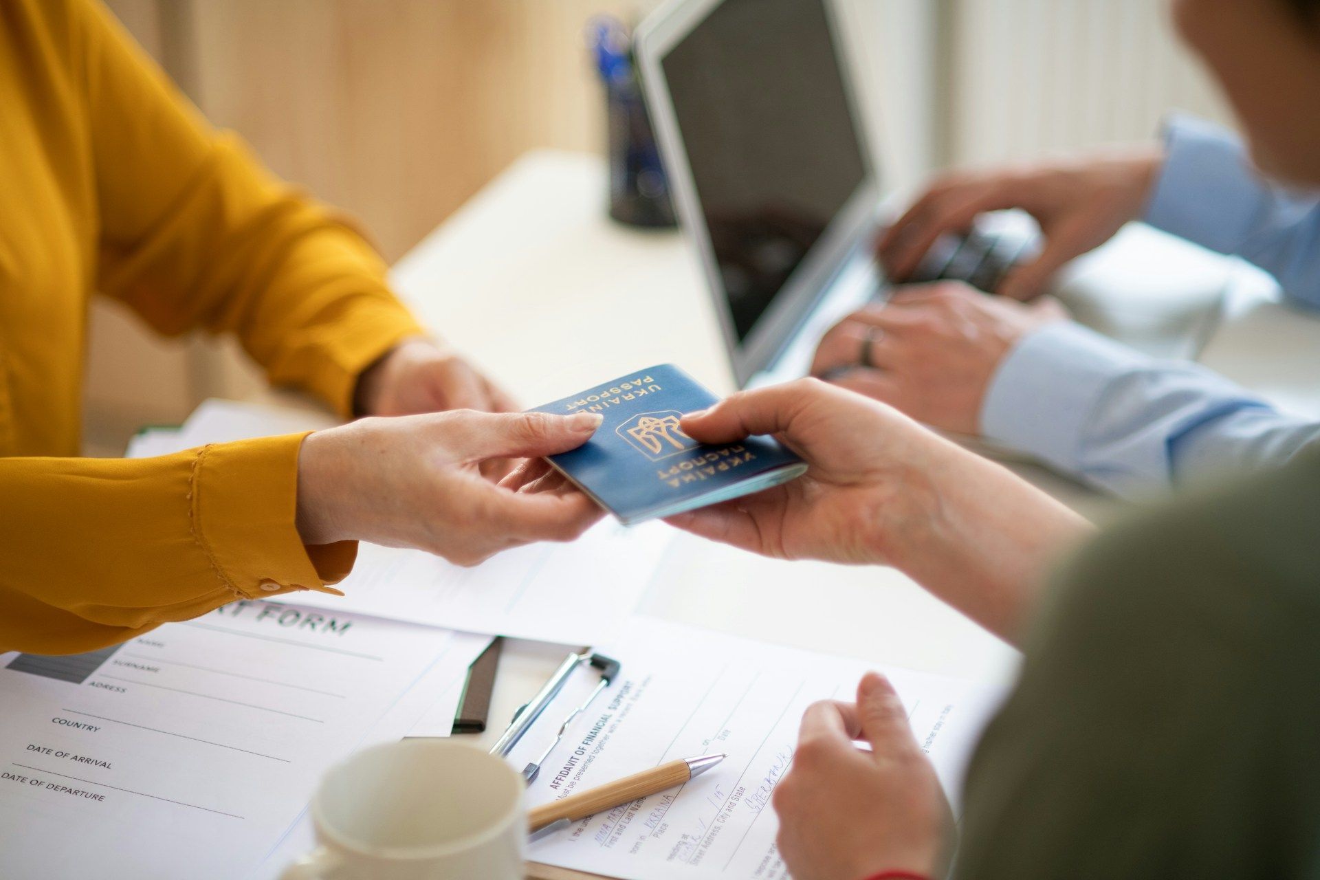A man in a wheelchair, working at a wooden desk with a laptop, mug, and documents.