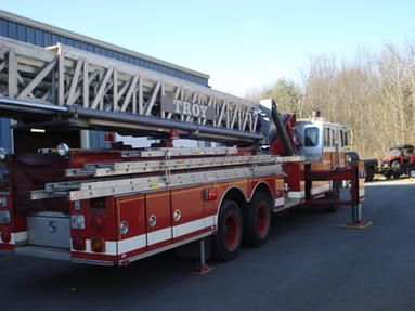 A red troy fire truck is parked in front of a building.