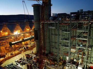 A large pipe is being lifted by a crane in a factory at night.