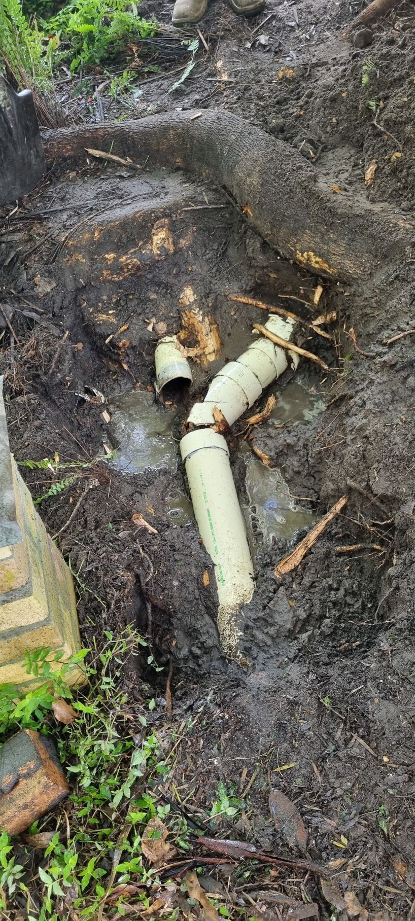 Broken White Pvc Pipes in A Muddy Area with Some Greenery — Hills 2 Ocean Plumbing in Yamba, NSW