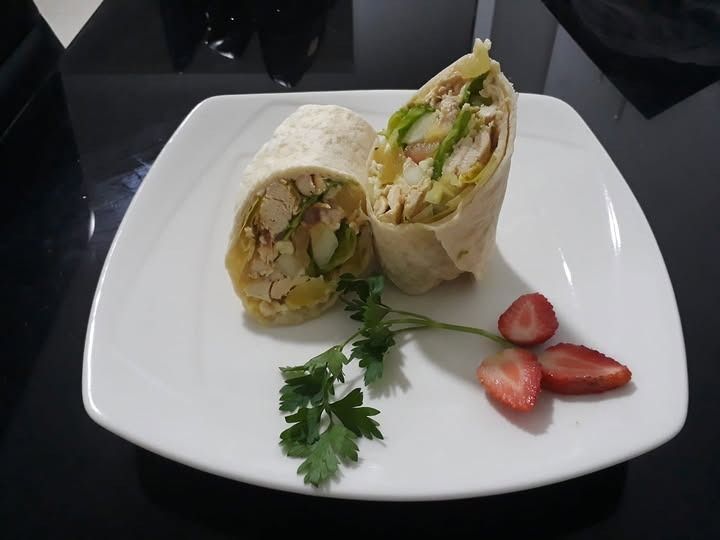 Wrap de pollo cortado por la mitad en un plato blanco con fresas y perejil.