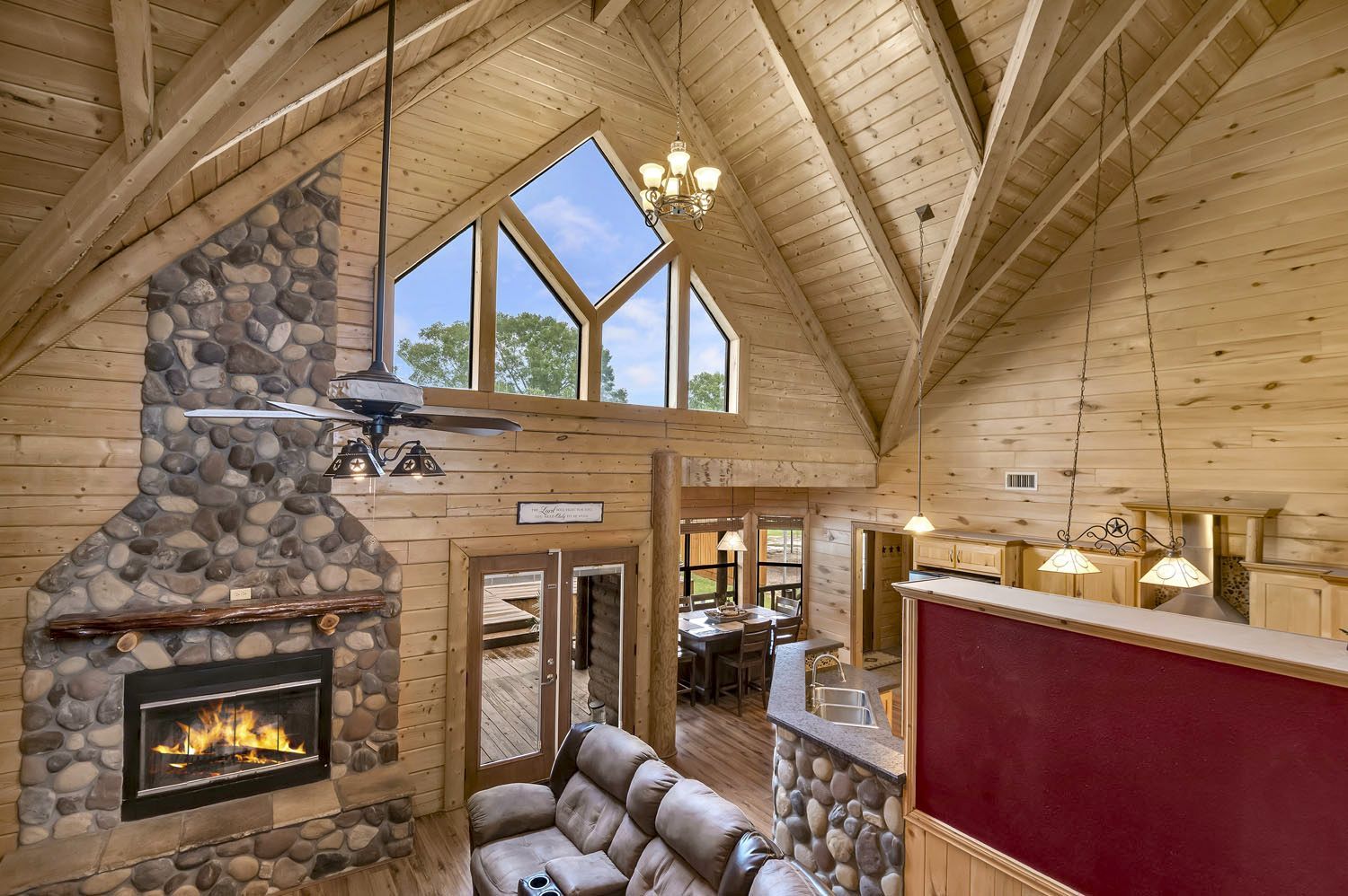 A living room in a log cabin with a fireplace and a ceiling fan.