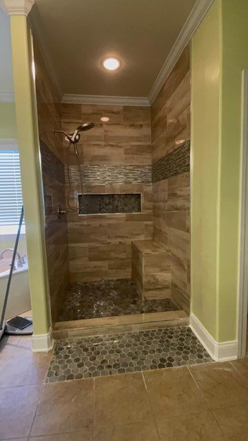 Shower with wood-look tile, pebble floor, and a bench; brown and gray tones, built-in shelf.