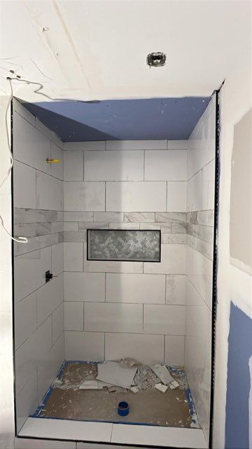 Bathroom shower under construction, tiled walls, blue ceiling, recessed shelf, and drain visible.