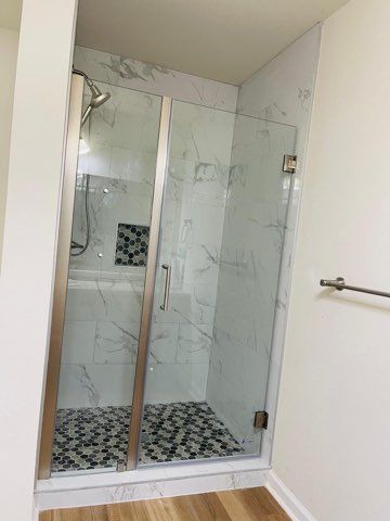 Shower stall with marble-like tile walls and a mosaic tile floor; glass door; silver fixtures.