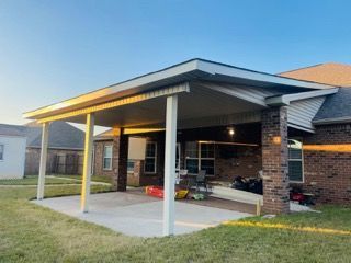 Covered patio attached to a brick house with concrete flooring, supported by white columns.
