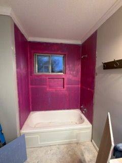 Bathroom renovation in progress; pink waterproof panels installed around a white bathtub and window.