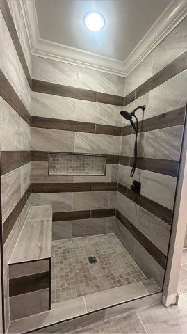 Shower with gray and brown striped tile, built-in bench, and black showerhead.