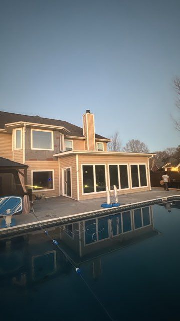 Poolside view of a beige house extension with large windows, chimney, and a swimming pool reflecting the structure.