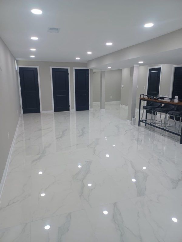 A spacious room with white marble floors and black doors, bar area on the right, recessed lighting.