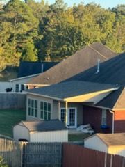Houses with dark roofs, surrounded by trees and a wooden fence. A shed is in the foreground.