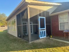 Screened-in porch attached to a house. Features include screen walls, a door, and a brick exterior.