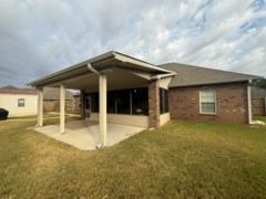 Backyard with covered patio, brown brick house, green grass, and cloudy sky.