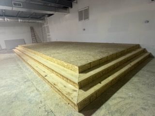 A three-tiered wooden platform, possibly a stage, in an unfinished room.