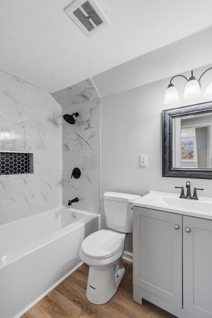 Modern bathroom with white tub, toilet, gray vanity, and marble tile shower surround.