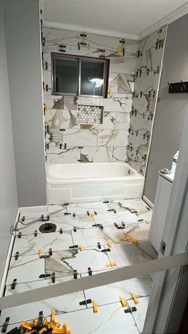 Bathroom under renovation with white marble-like tiles and leveling spacers in use.