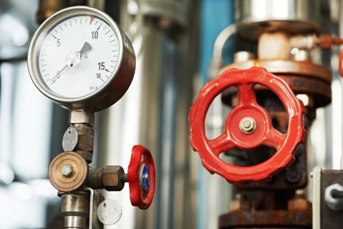 A close up of a pressure gauge and a red valve in a factory.