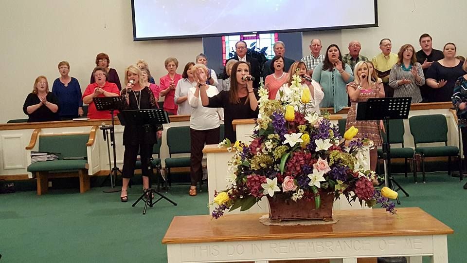 A group of people singing in a church with a basket of flowers on a table in front of them.