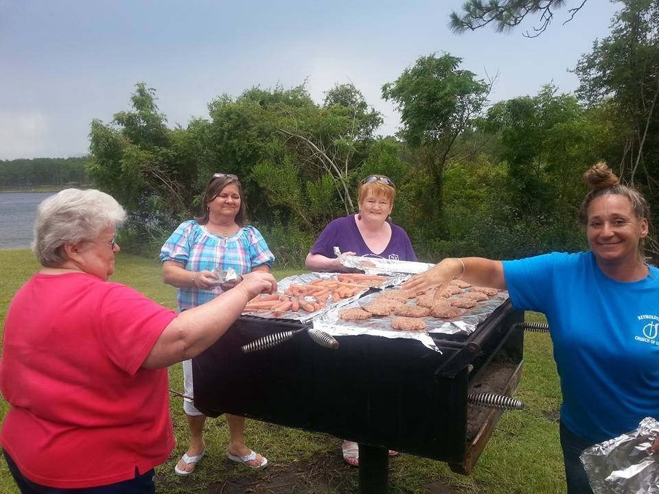 A group of women are standing around a grill with meat on it.