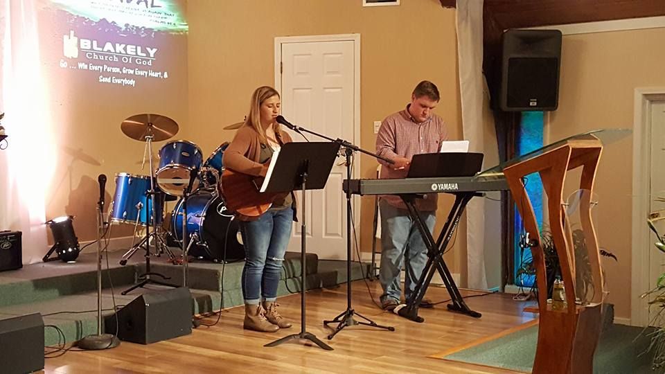 A woman is singing into a microphone while a man plays a keyboard.