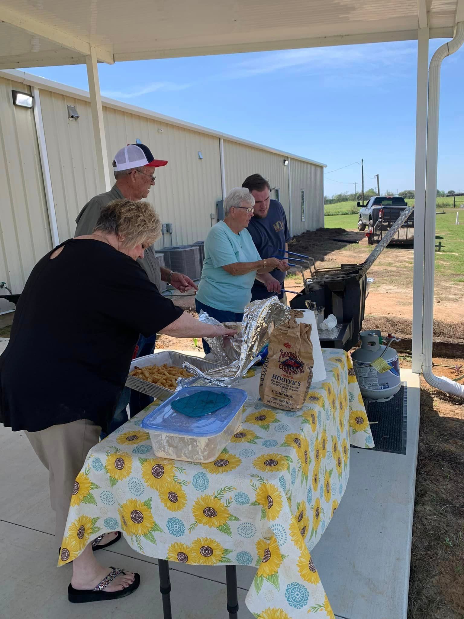 A group of people are standing around a table with a sunflower tablecloth.