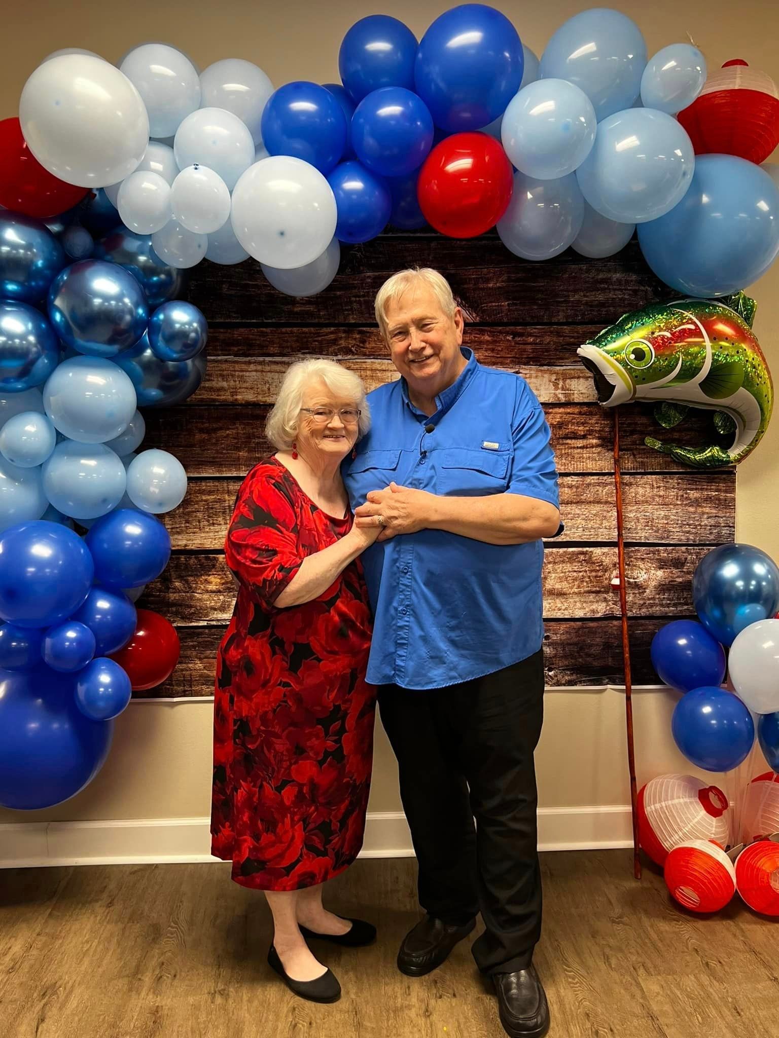 A man and a woman are standing in front of a wall decorated with balloons.