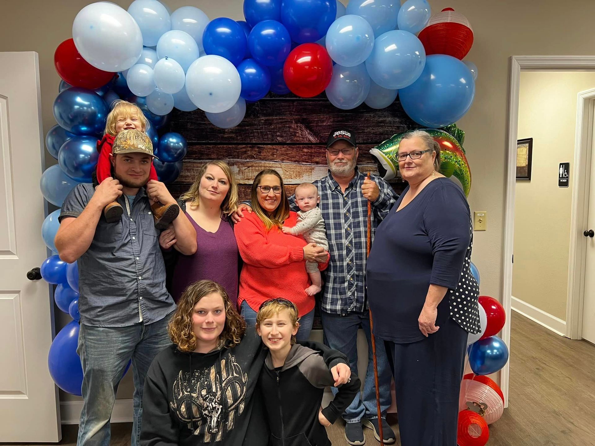 A large family is posing for a picture in front of balloons.