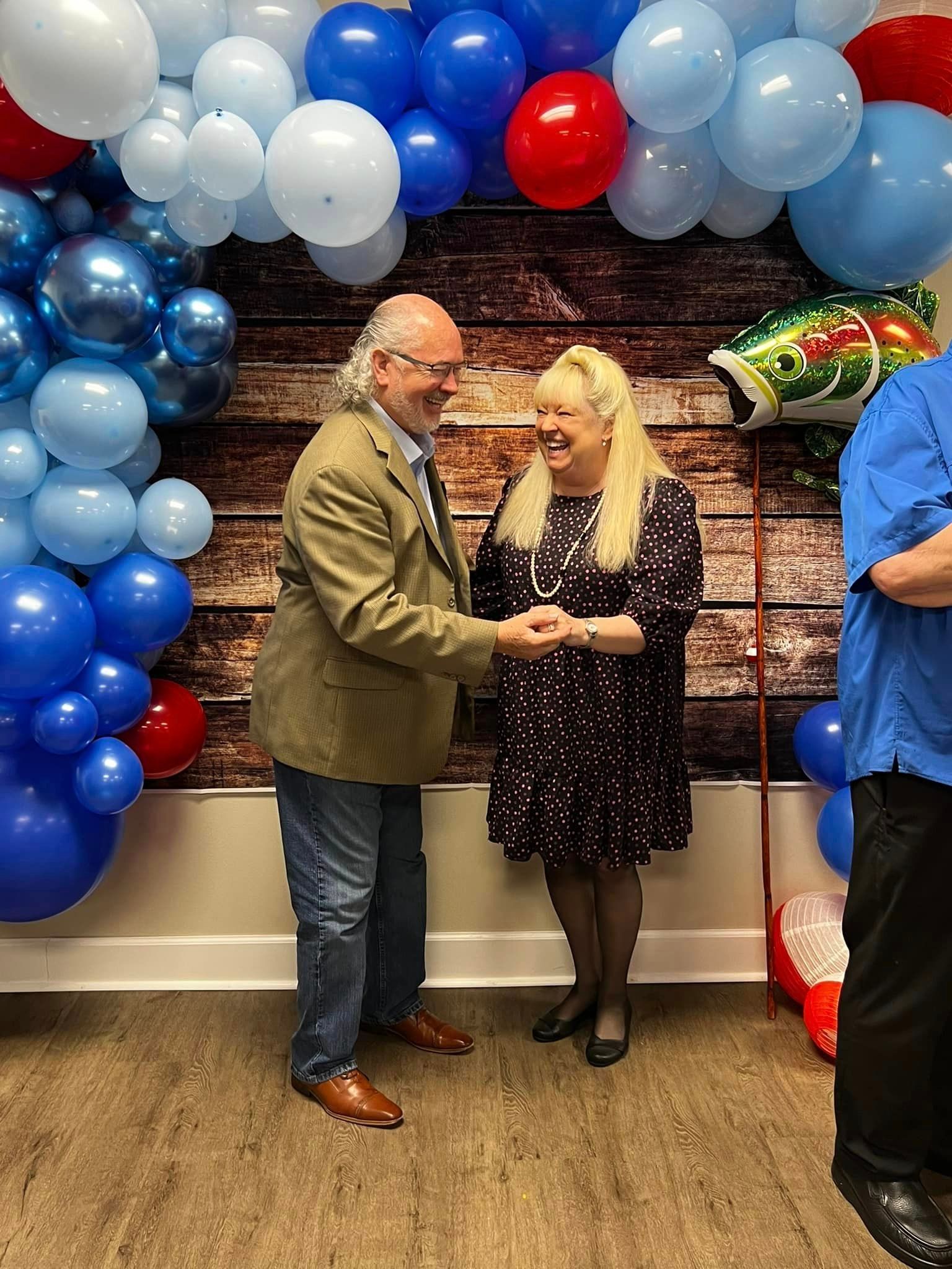 A man and a woman are holding hands in front of a wall of balloons.
