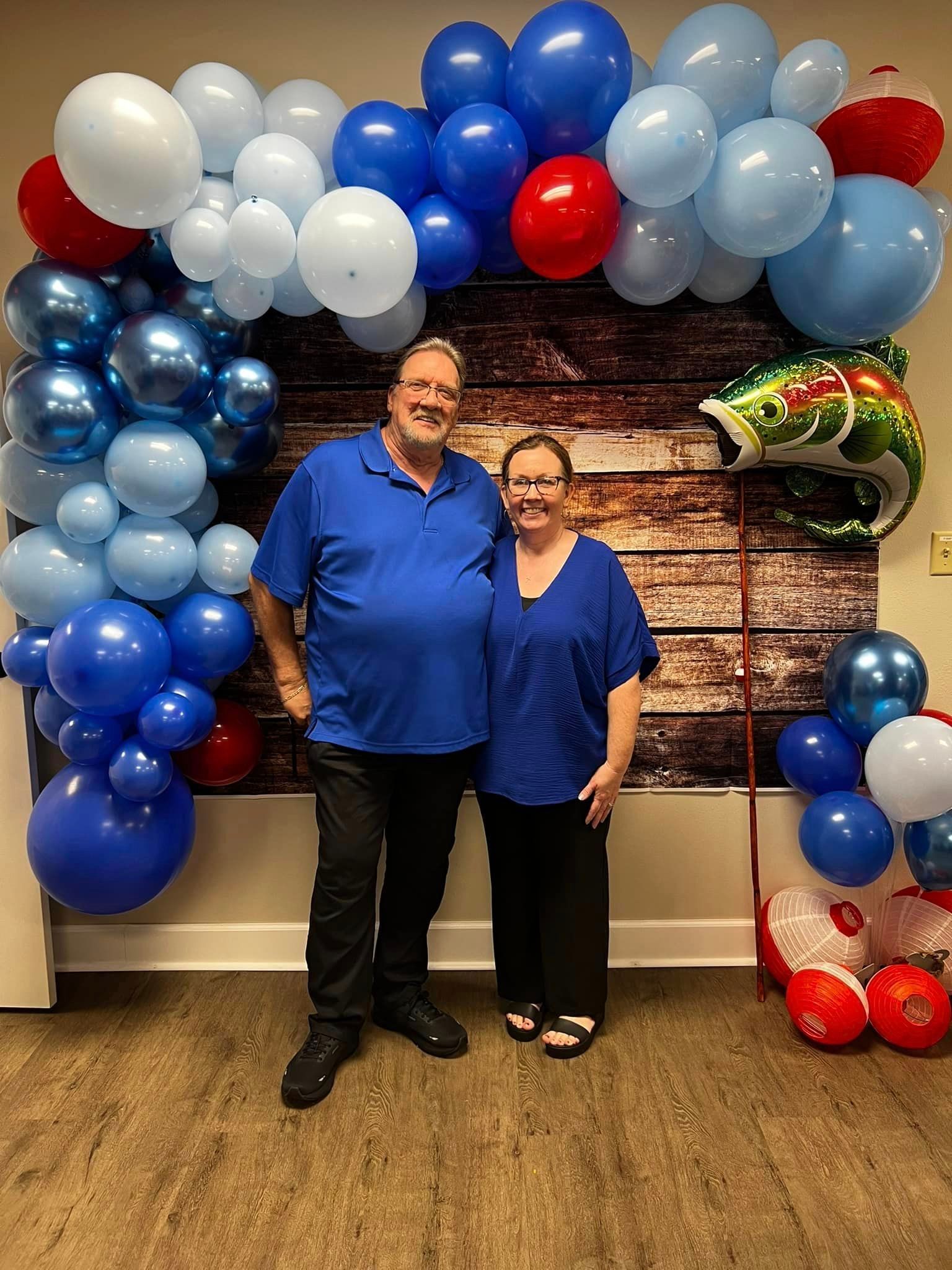 A man and a woman are standing in front of a wall decorated with blue and red balloons.