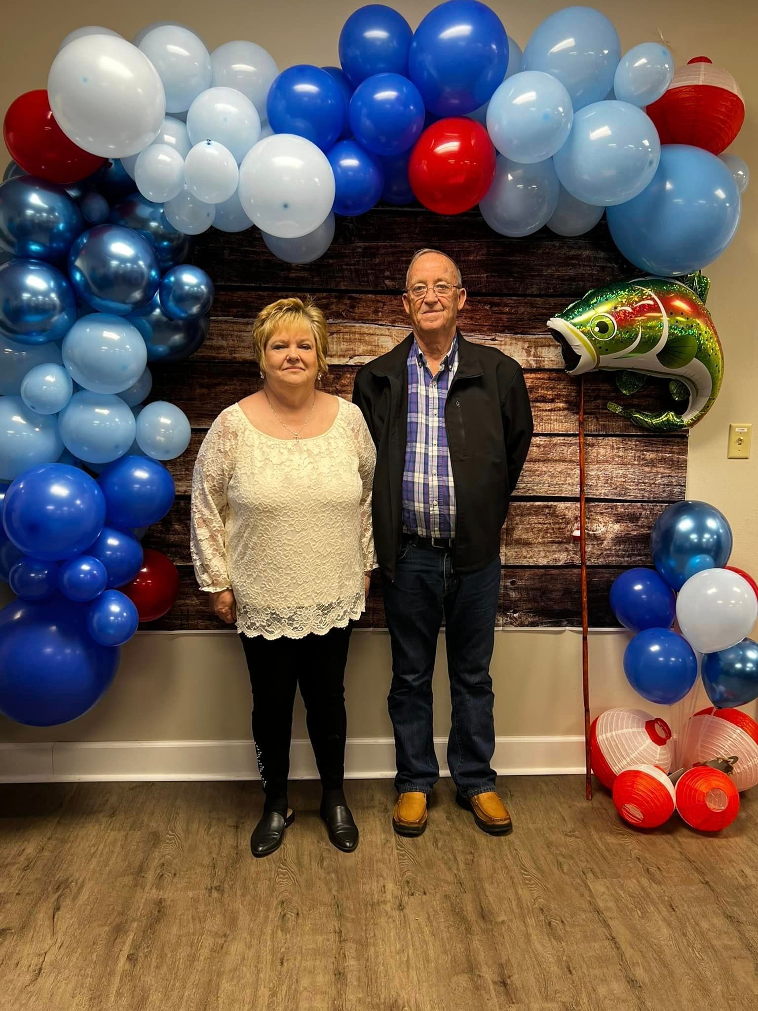 A man and a woman are standing in front of a wall decorated with blue and red balloons.