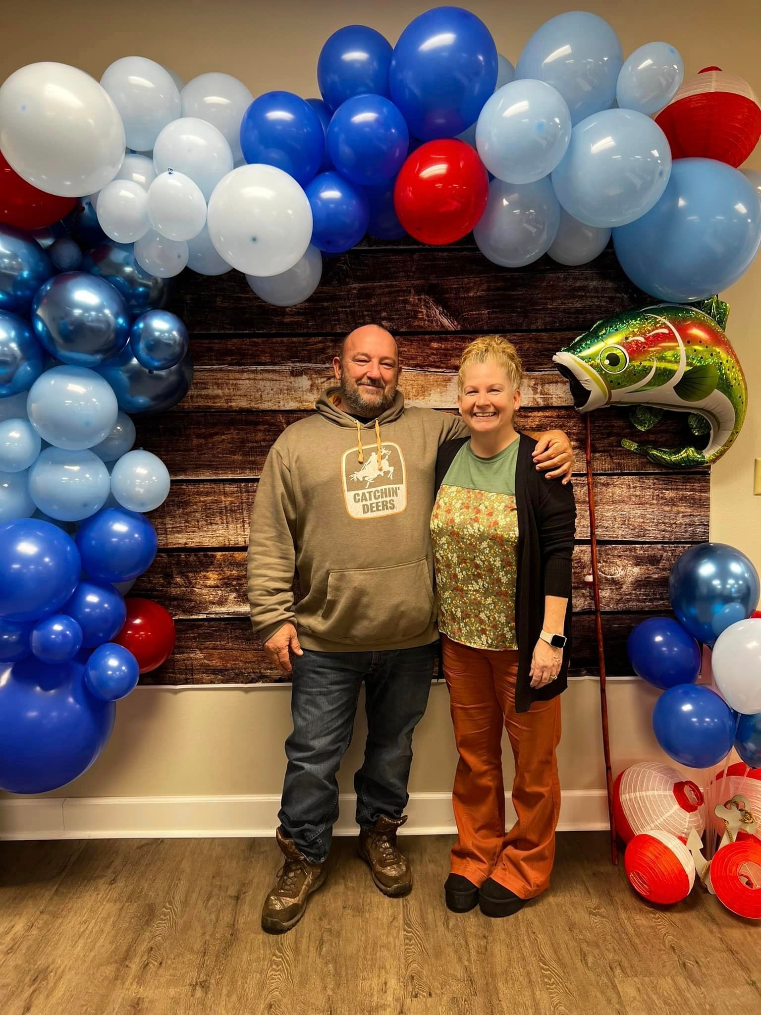 A man and a woman are standing in front of a wall decorated with balloons.