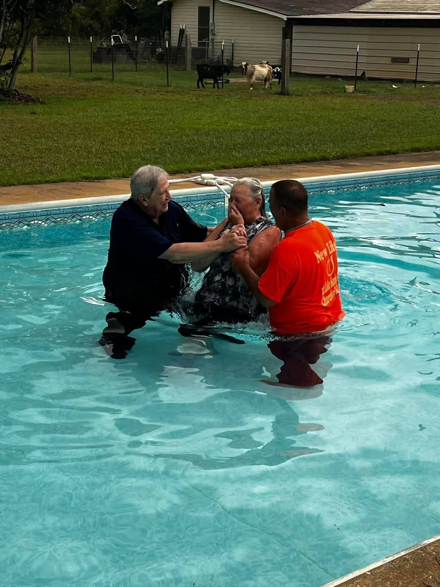 A man in an orange shirt is baptizing another man in a pool