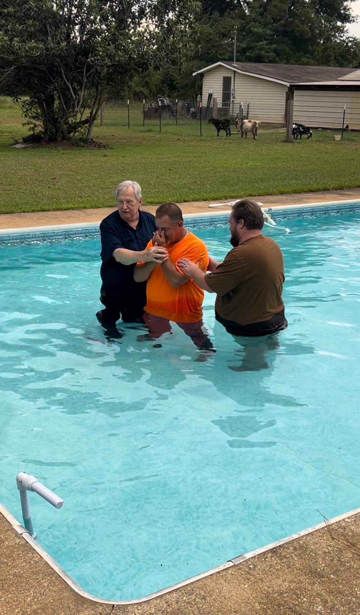 Three men are baptizing a man in a swimming pool.