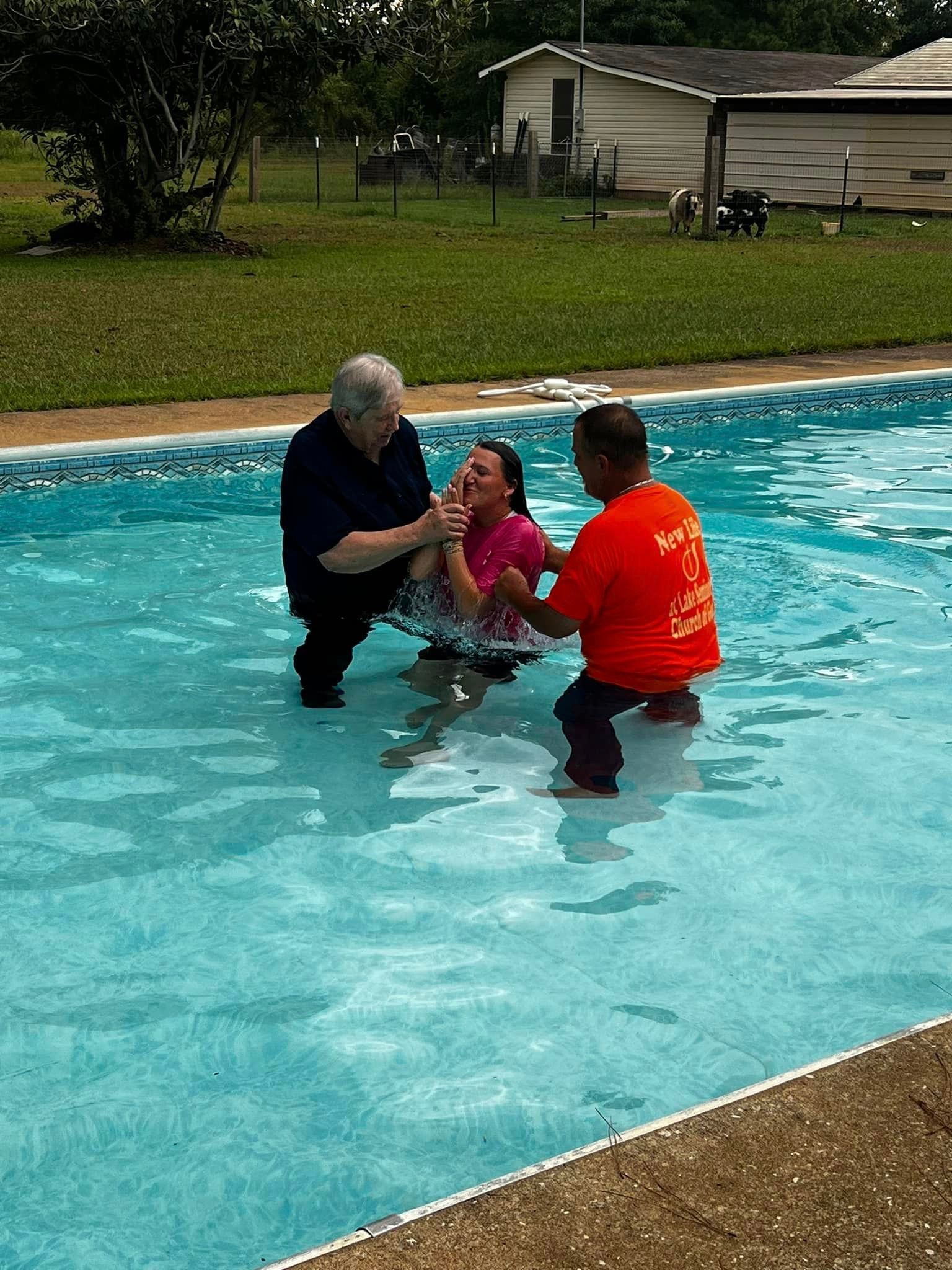 A man in an orange shirt is baptizing a girl in a pool