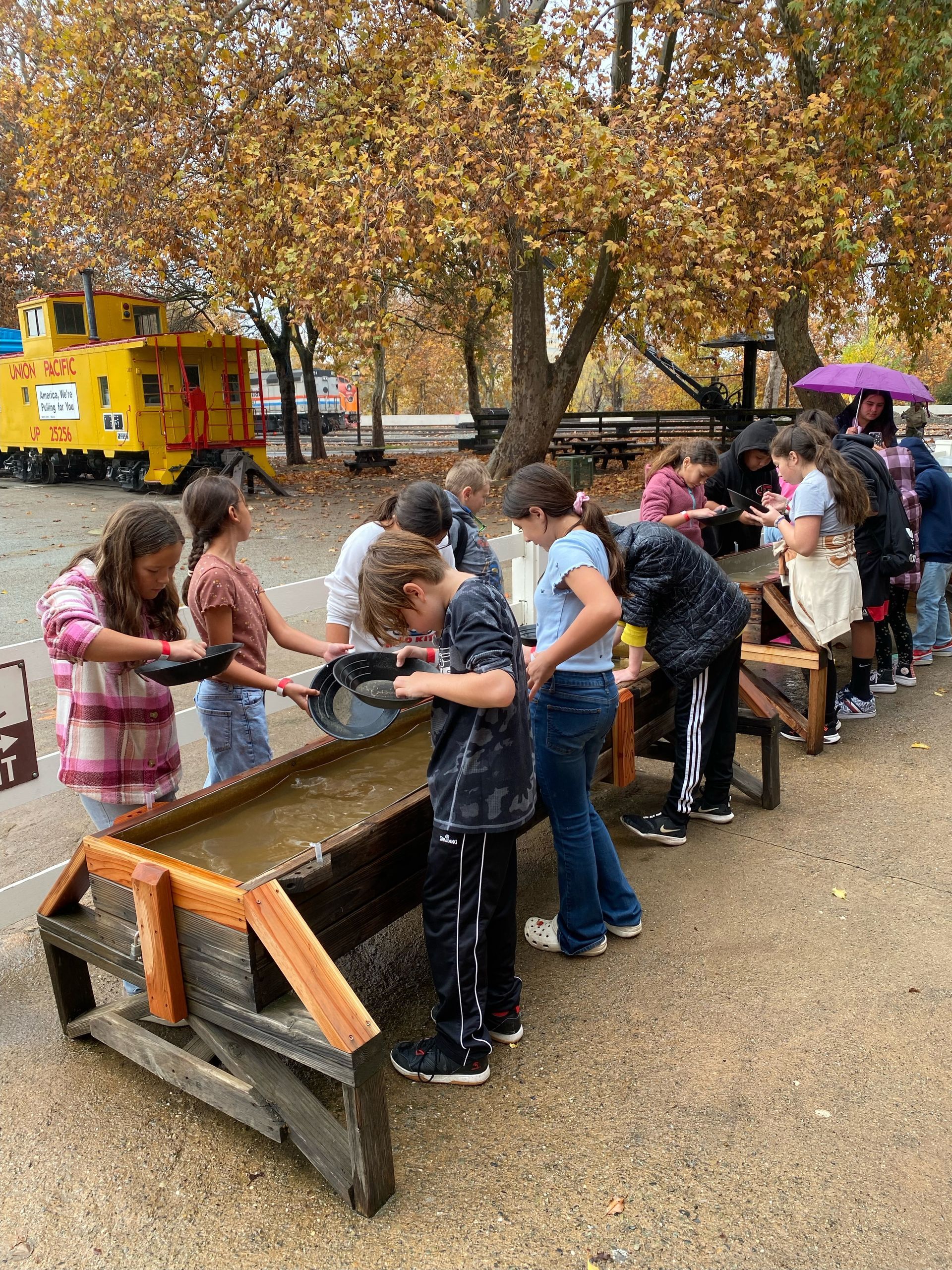 A group of children are standing around a wooden table.
