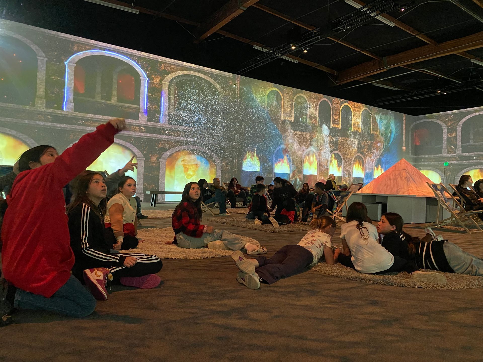 A group of children are sitting on the floor in front of a large screen.