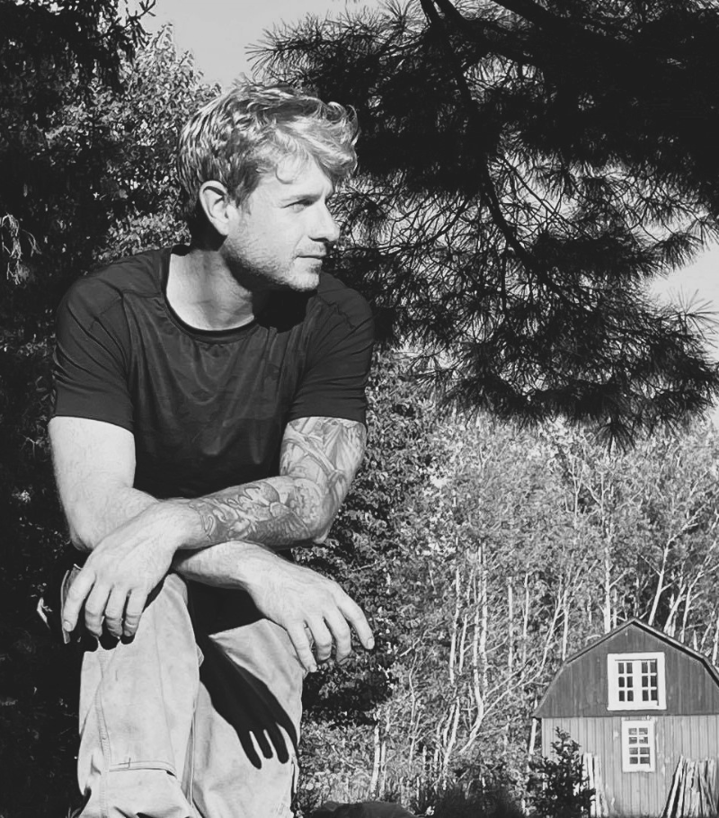 Une photo en noir et blanc d'un homme assis devant une grange