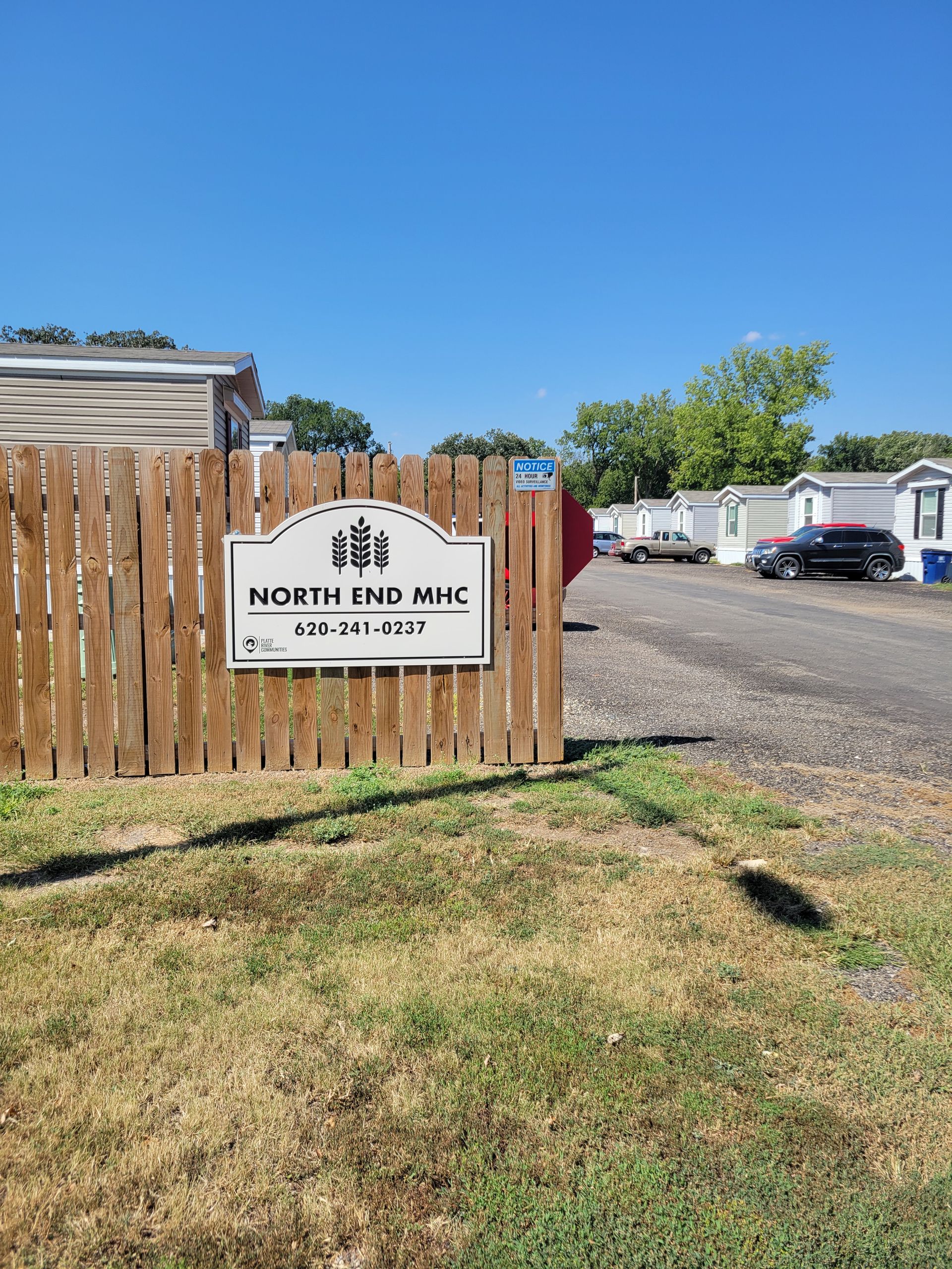 A wooden fence with a sign on it in front of a mobile home park.
