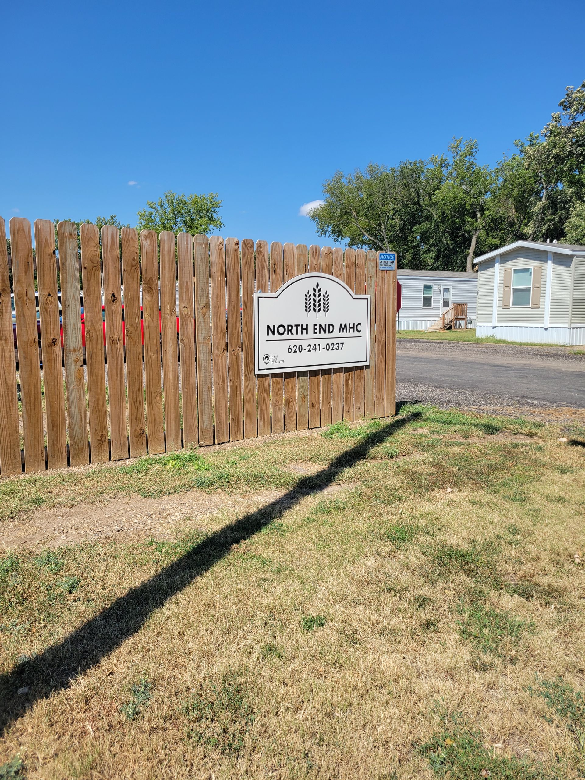 A wooden fence with a sign on it in front of a mobile home park.