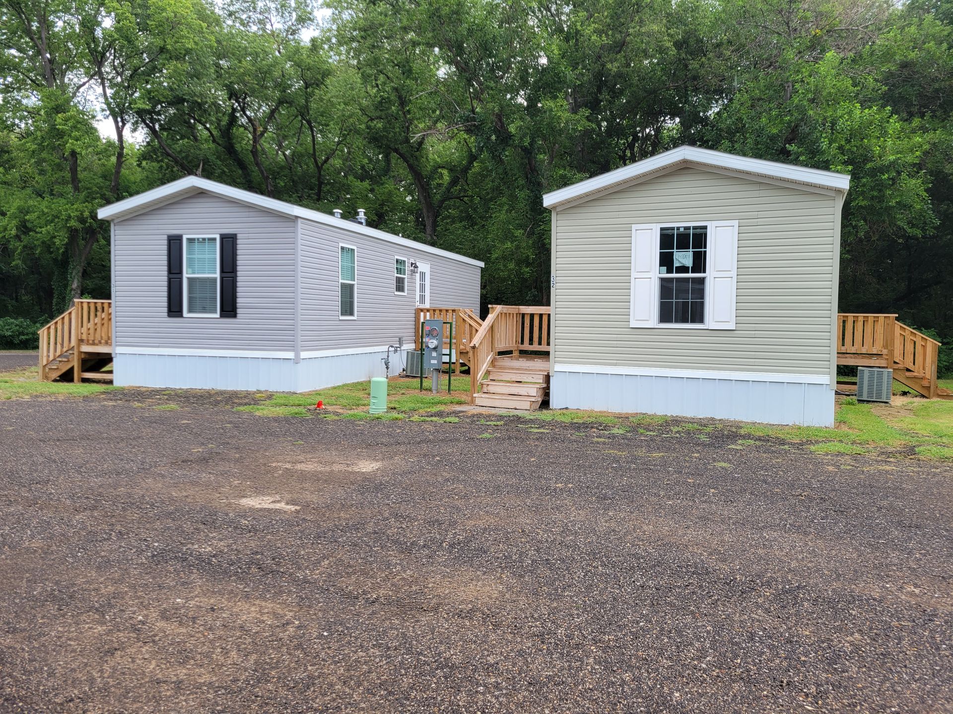 Two mobile homes are parked next to each other in a gravel lot.