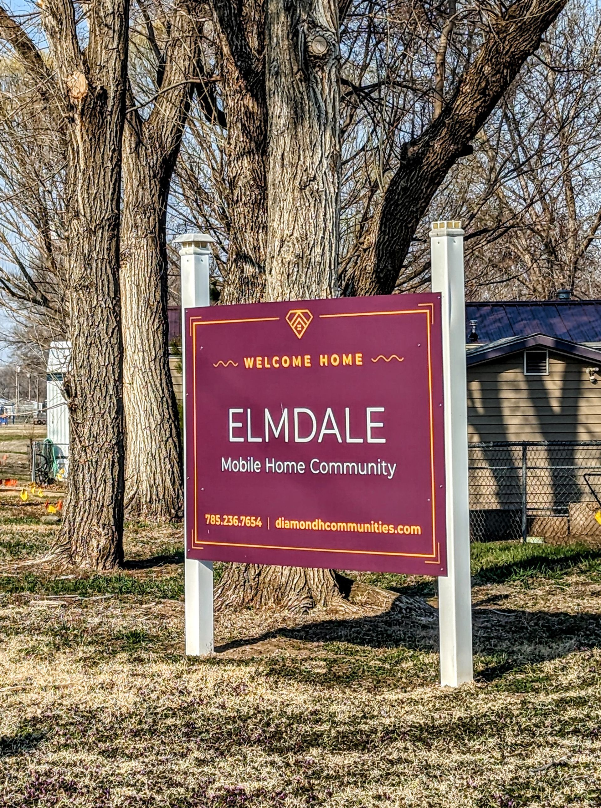A sign for elmdale is sitting in the middle of a grassy field.