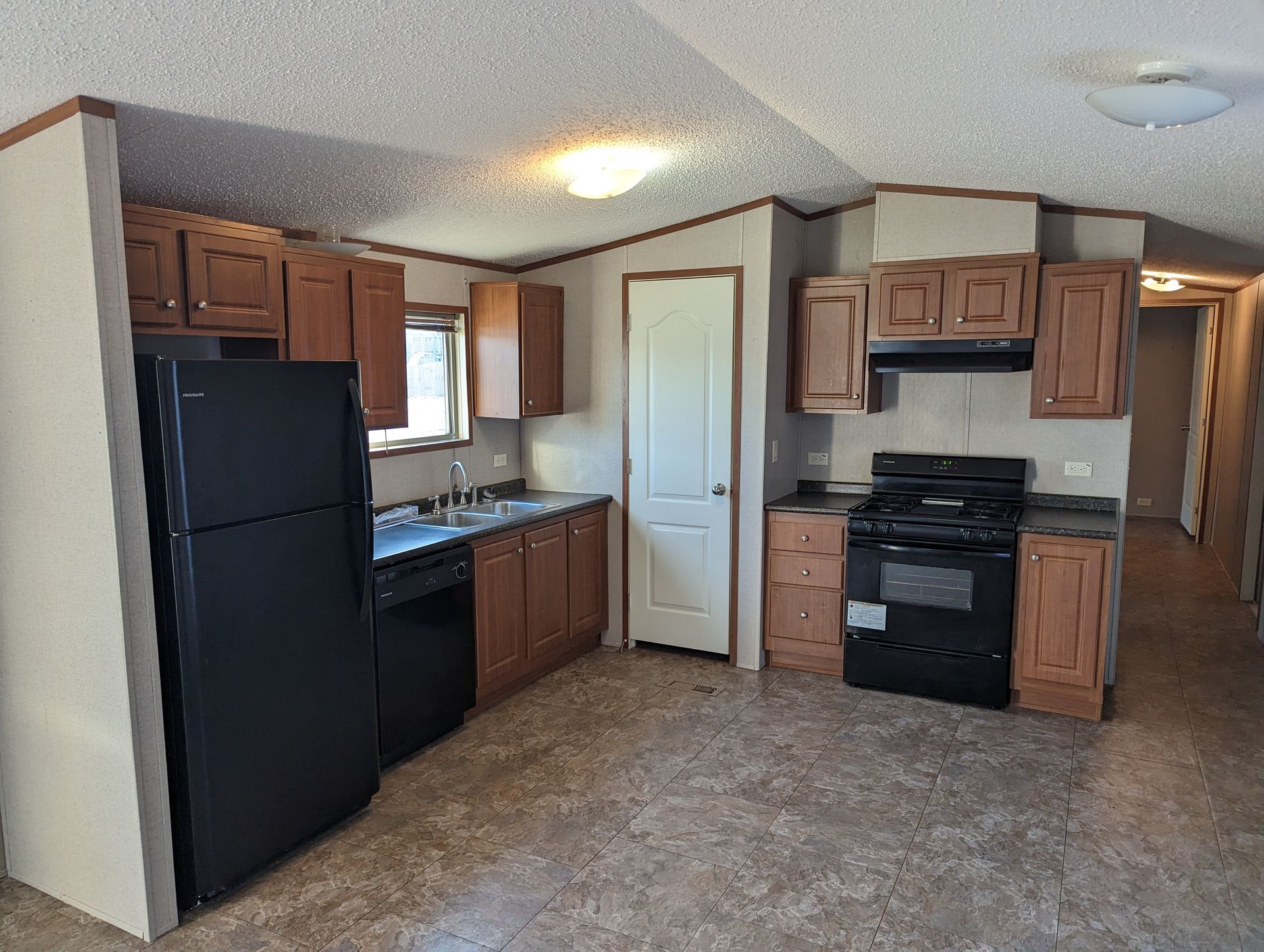 A kitchen in a mobile home with a black refrigerator , stove and dishwasher.