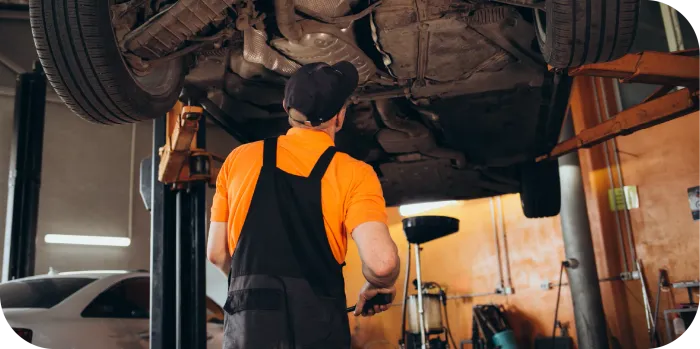 A man is writing on a clipboard while looking under the hood of a car.