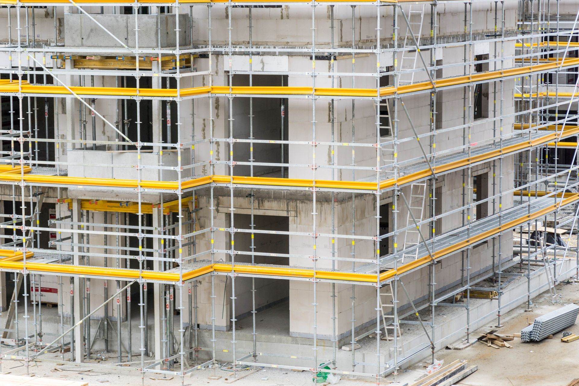 Multi-story concrete building under construction with scaffolding and yellow safety rails surroundin